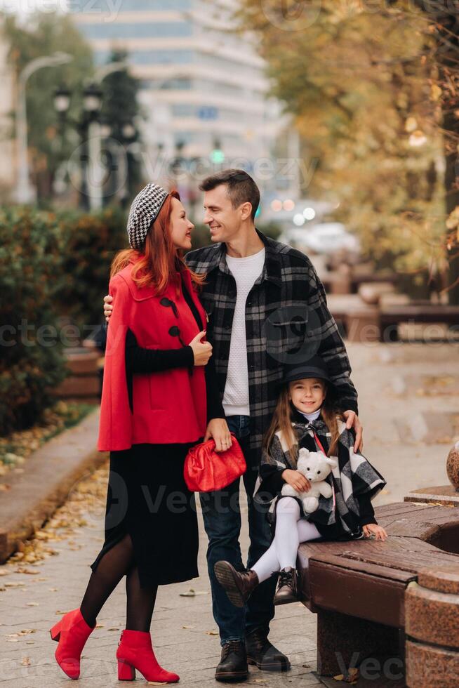 A stylish family of three strolls through the autumn city posing for a photographer . Dad, mom and daughter in the autumn city photo