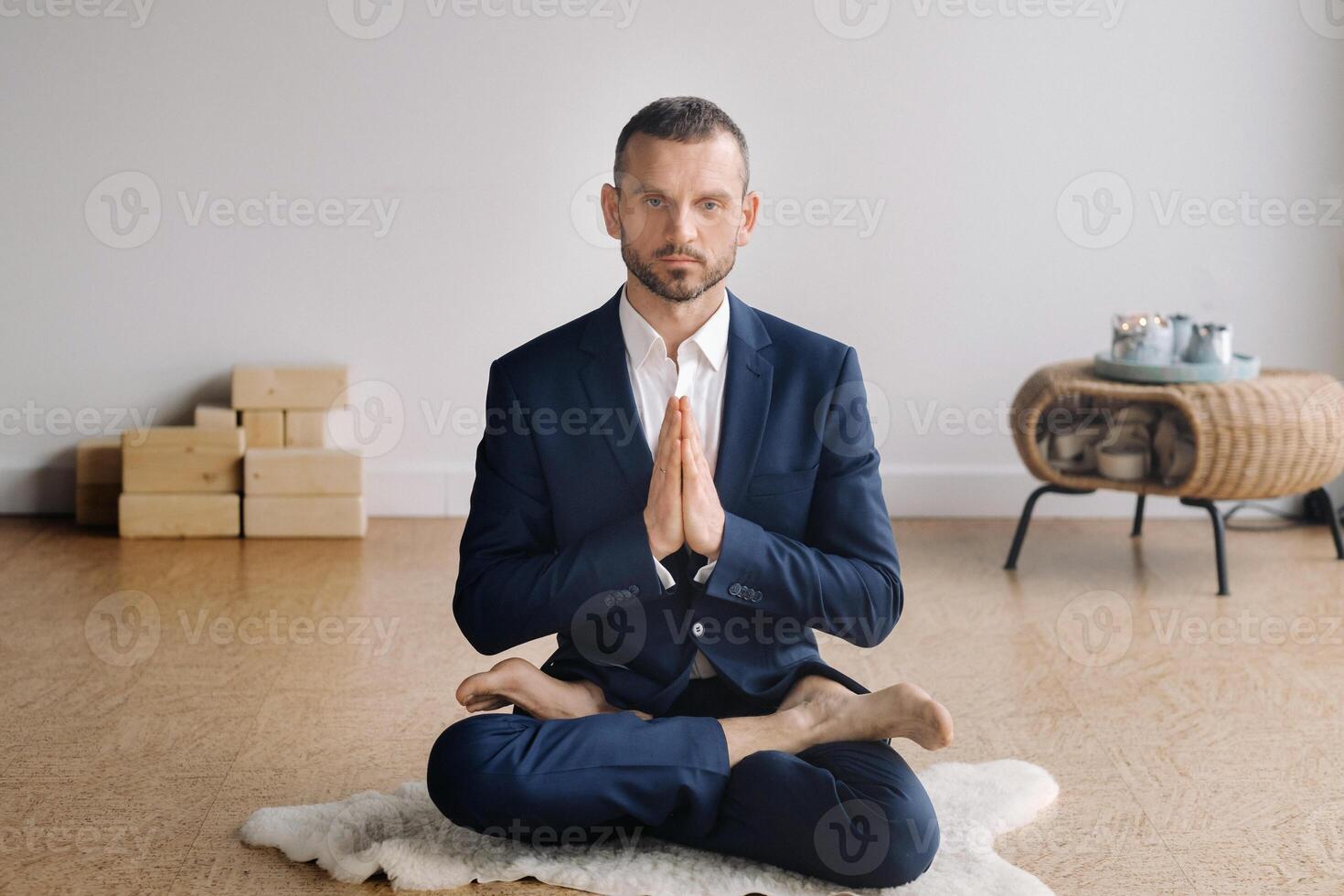 A man in a strict suit does Yoga while sitting in a fitness room photo