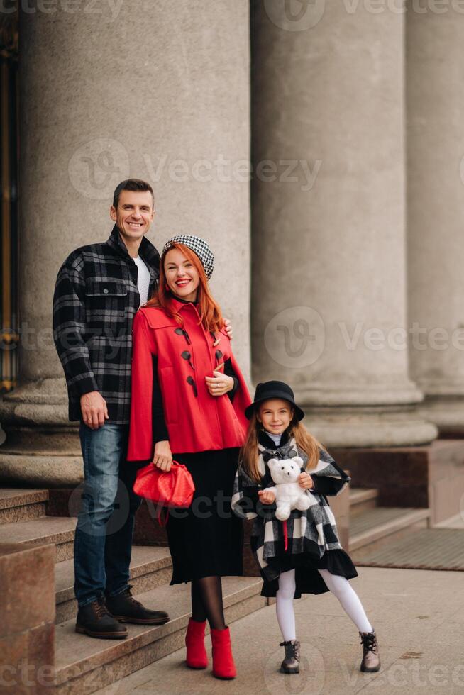 A stylish family of three is in town in the fall, and the girl with the stuffed toy is cheerful photo