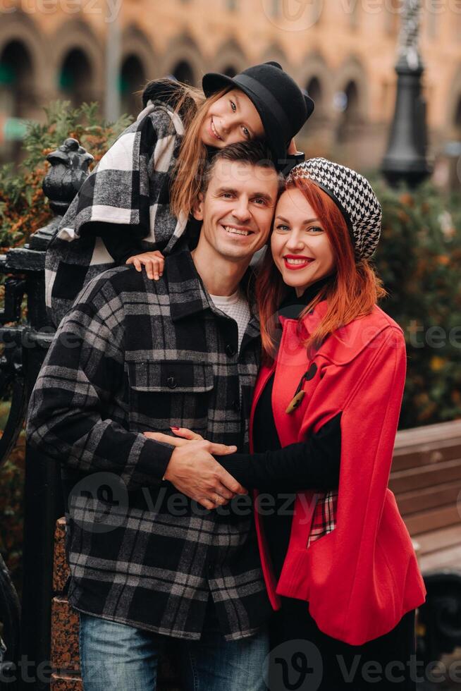 A stylish family of three strolls through the autumn city posing for a photographer . Dad, mom and daughter in the autumn city photo