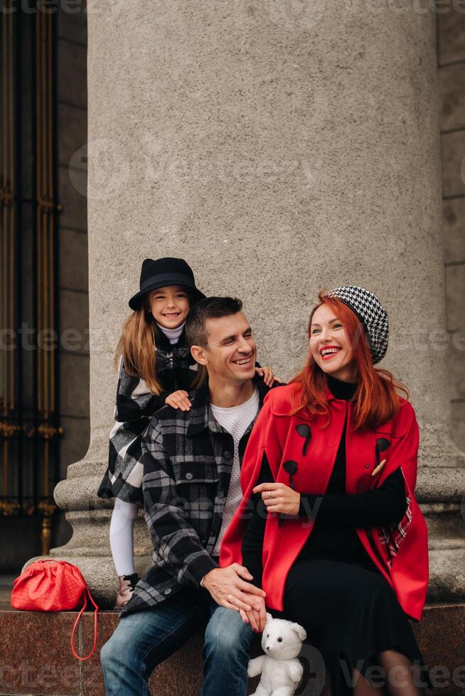 un elegante familia de Tres paseos mediante el otoño ciudad posando para un fotógrafo . papá, mamá y hija en el otoño ciudad foto