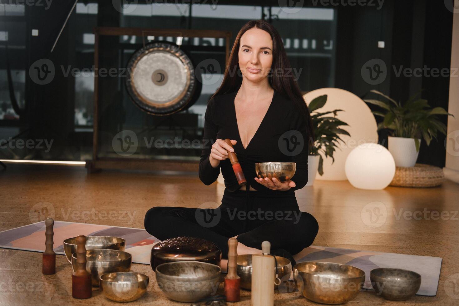 A woman in the lotus position using a singing bowl indoors . Relaxation and meditation. Sound therapy, alternative medicine. Buddhist healing practices photo