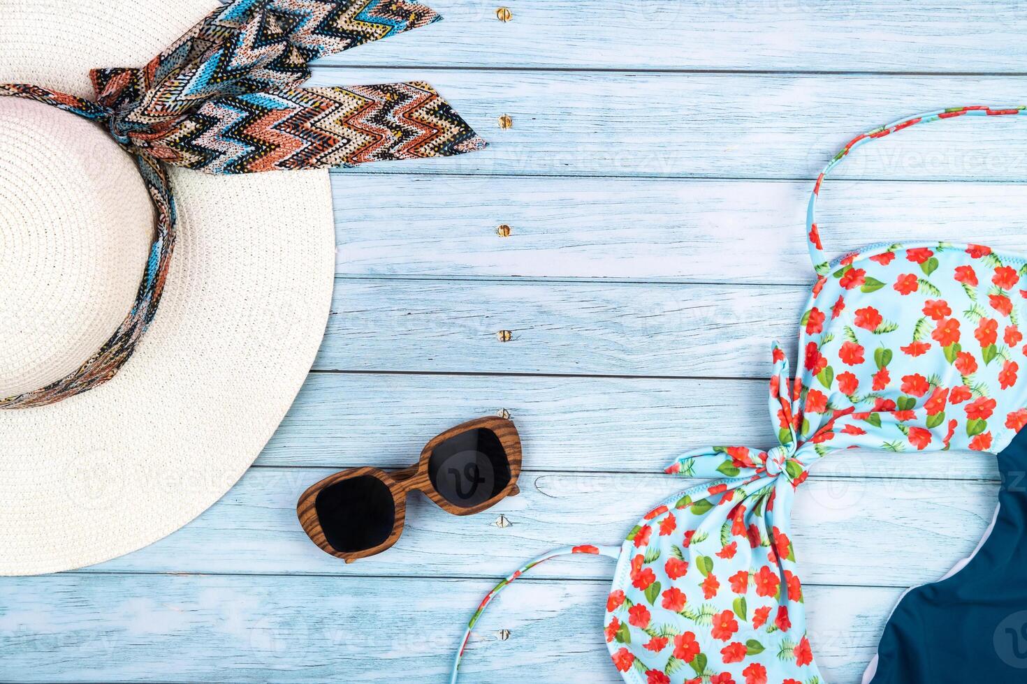 Top view of a straw white hat with glasses and a swimsuit, lying on a blue wooden background.Summer vacation concept photo