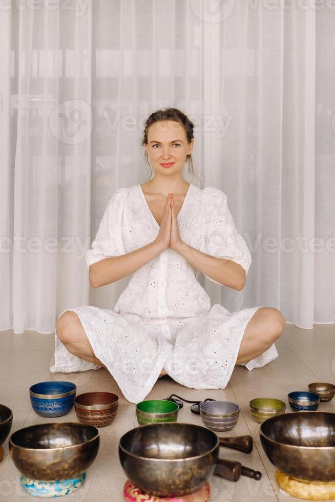 A woman sits with Tibetan bowls in the lotus position before doing yoga in the gym photo