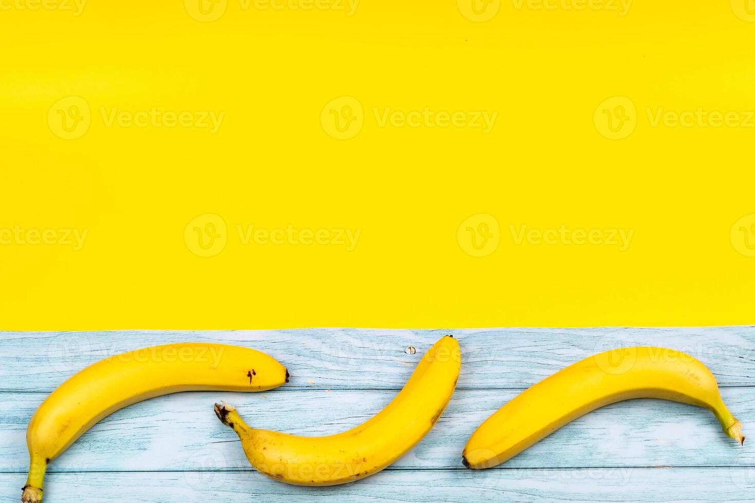 Yellow bananas lie on a blue wooden background and a yellow background photo