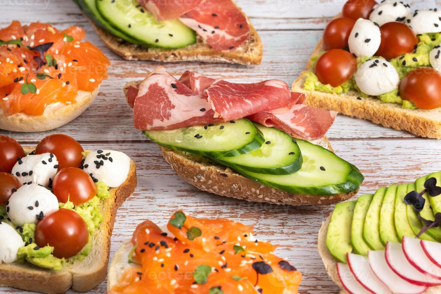 An assortment of sandwiches with fish, cheese, meat and vegetables lay on the wooden table photo