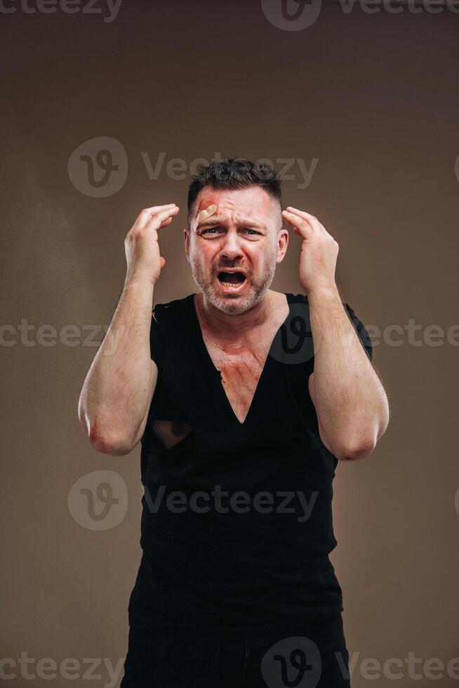 Against a gray background stands a battered angry man in a black T-shirt with wounds photo