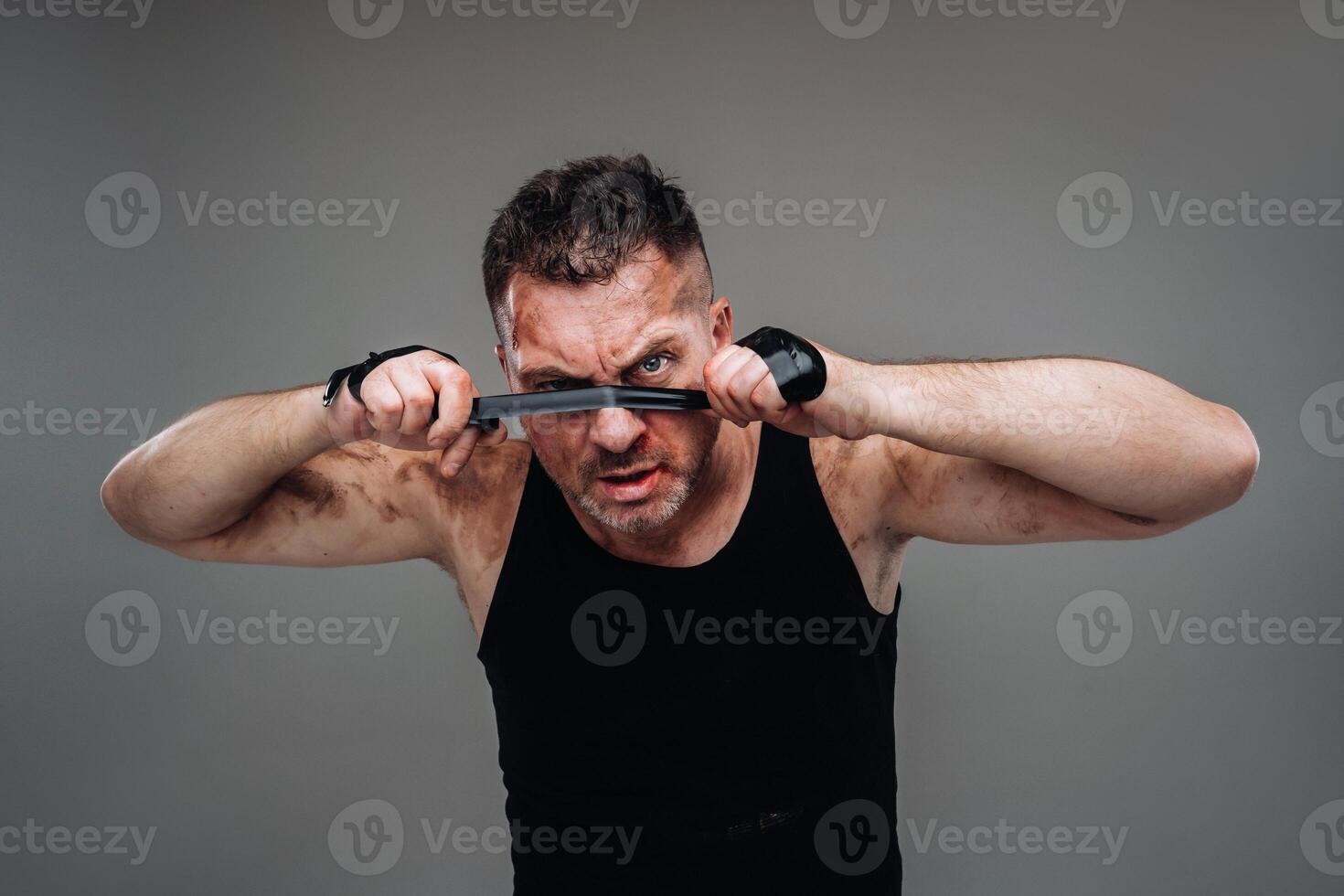 on a gray background stands a battered man in a black T shirt looking like a fighter and preparing for a fight photo