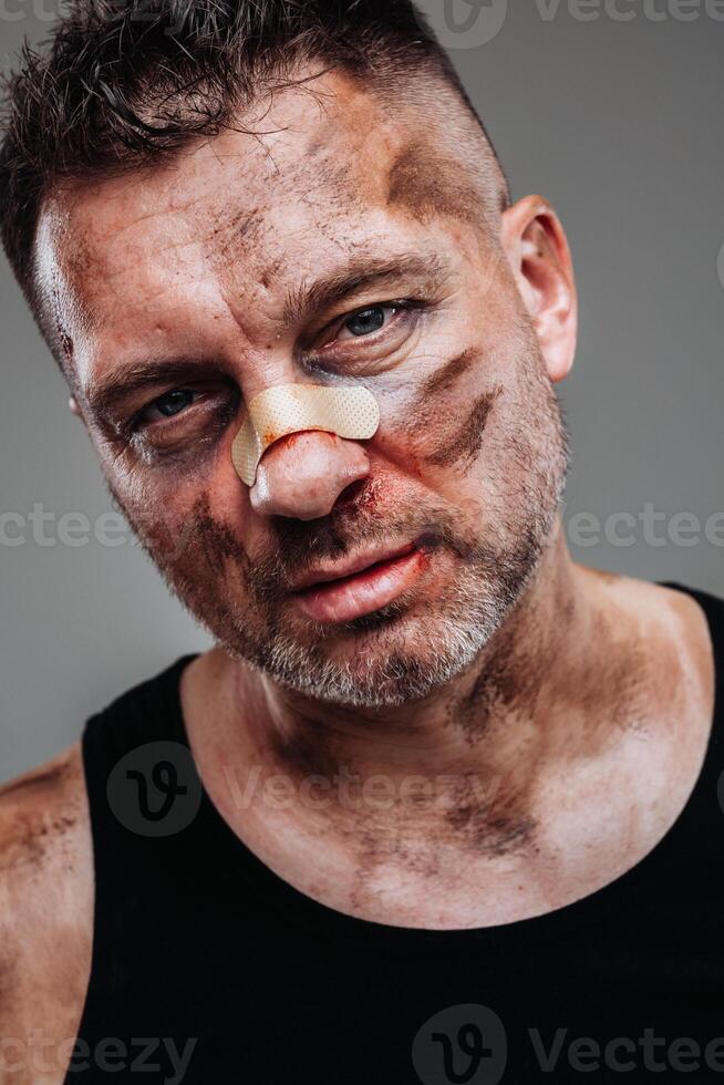 a battered man in a black T shirt who looks like a drug addict and a drunk stands against a gray background photo