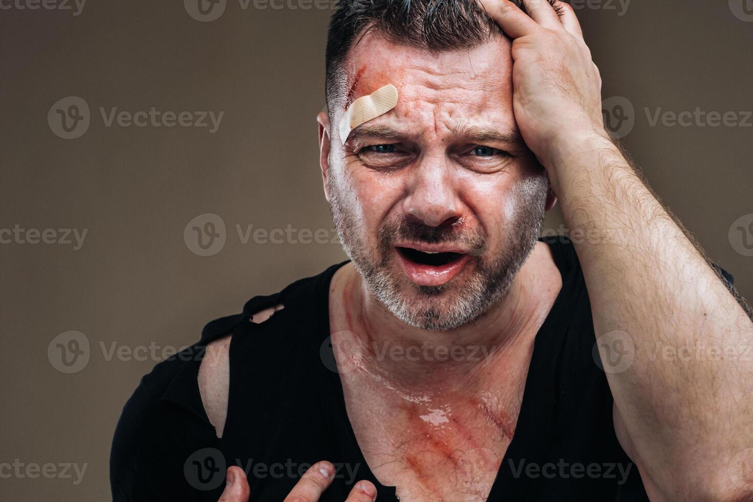 Against a gray background stands a battered angry man in a black T-shirt with wounds photo