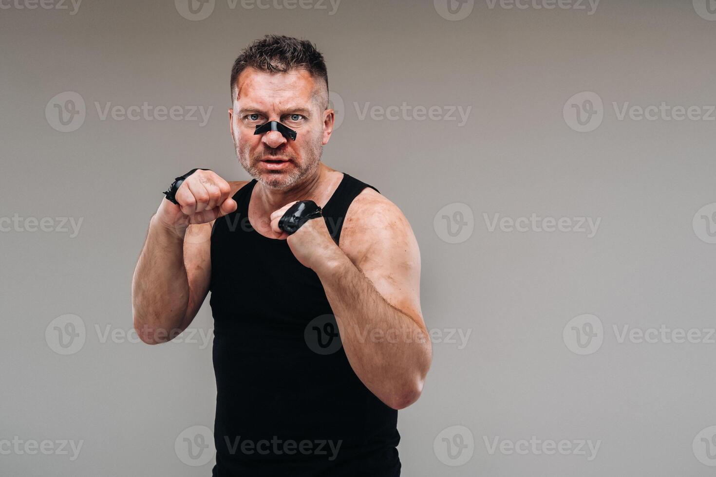 on a gray background stands a battered man in a black T shirt looking like a fighter and preparing for a fight photo