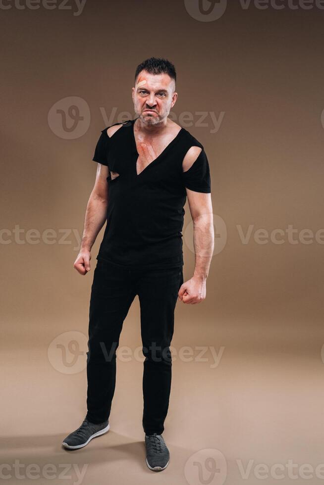 Against a gray background stands a battered angry man in a black T-shirt with wounds photo