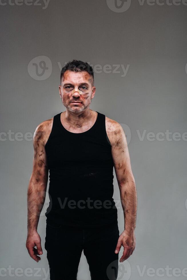 a battered man in a black T shirt who looks like a drug addict and a drunk stands against a gray background photo