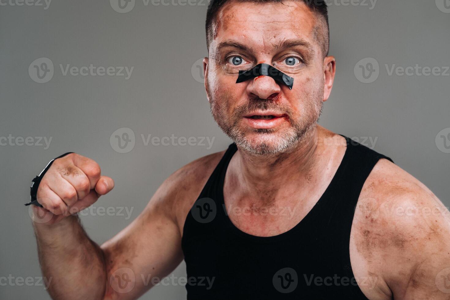 on a gray background stands a battered man in a black T shirt looking like a fighter and preparing for a fight photo