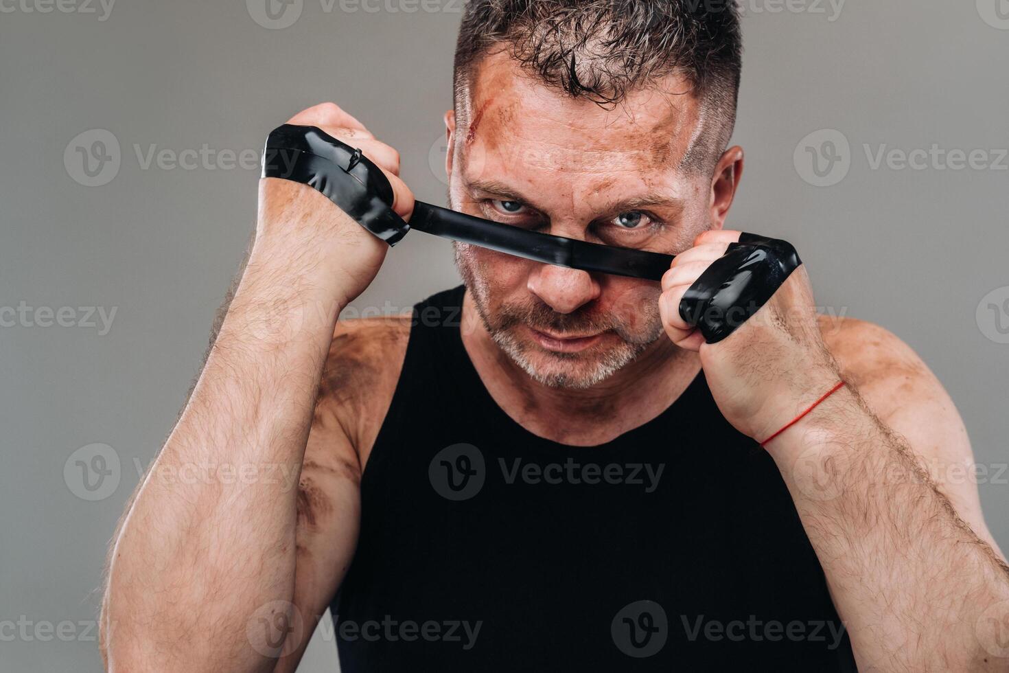 on a gray background stands a battered man in a black T shirt looking like a fighter and preparing for a fight photo