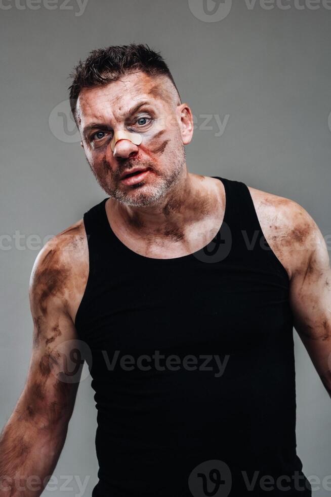 a battered man in a black T shirt who looks like a drug addict and a drunk stands against a gray background photo