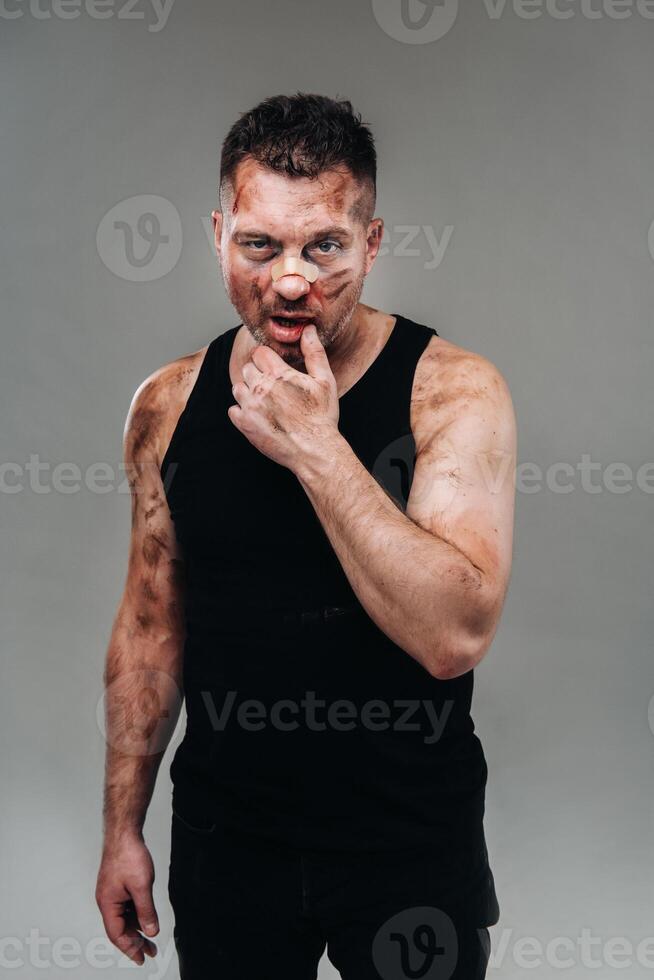 a battered man in a black T shirt who looks like a drug addict and a drunk stands against a gray background photo