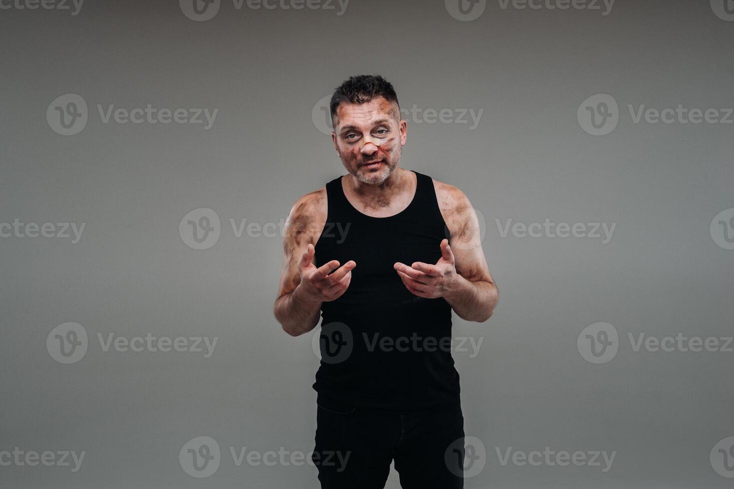 a battered man in a black T shirt who looks like a drug addict and a drunk stands against a gray background photo