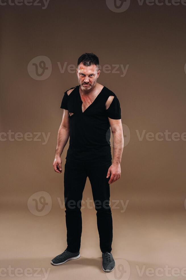 Against a gray background stands a battered angry man in a black T-shirt with wounds photo