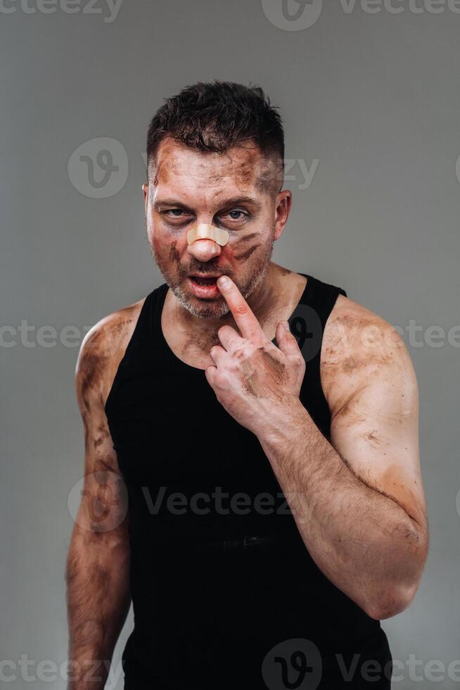 a battered man in a black T shirt who looks like a drug addict and a drunk stands against a gray background photo