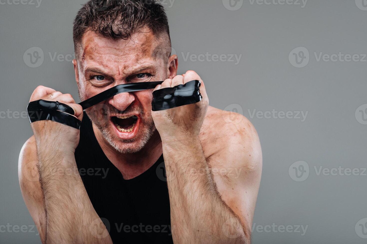 on a gray background stands a battered man in a black T shirt looking like a fighter and preparing for a fight photo