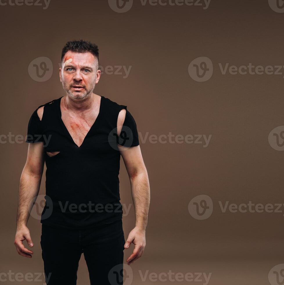 Against a gray background stands a battered angry man in a black T-shirt with wounds photo