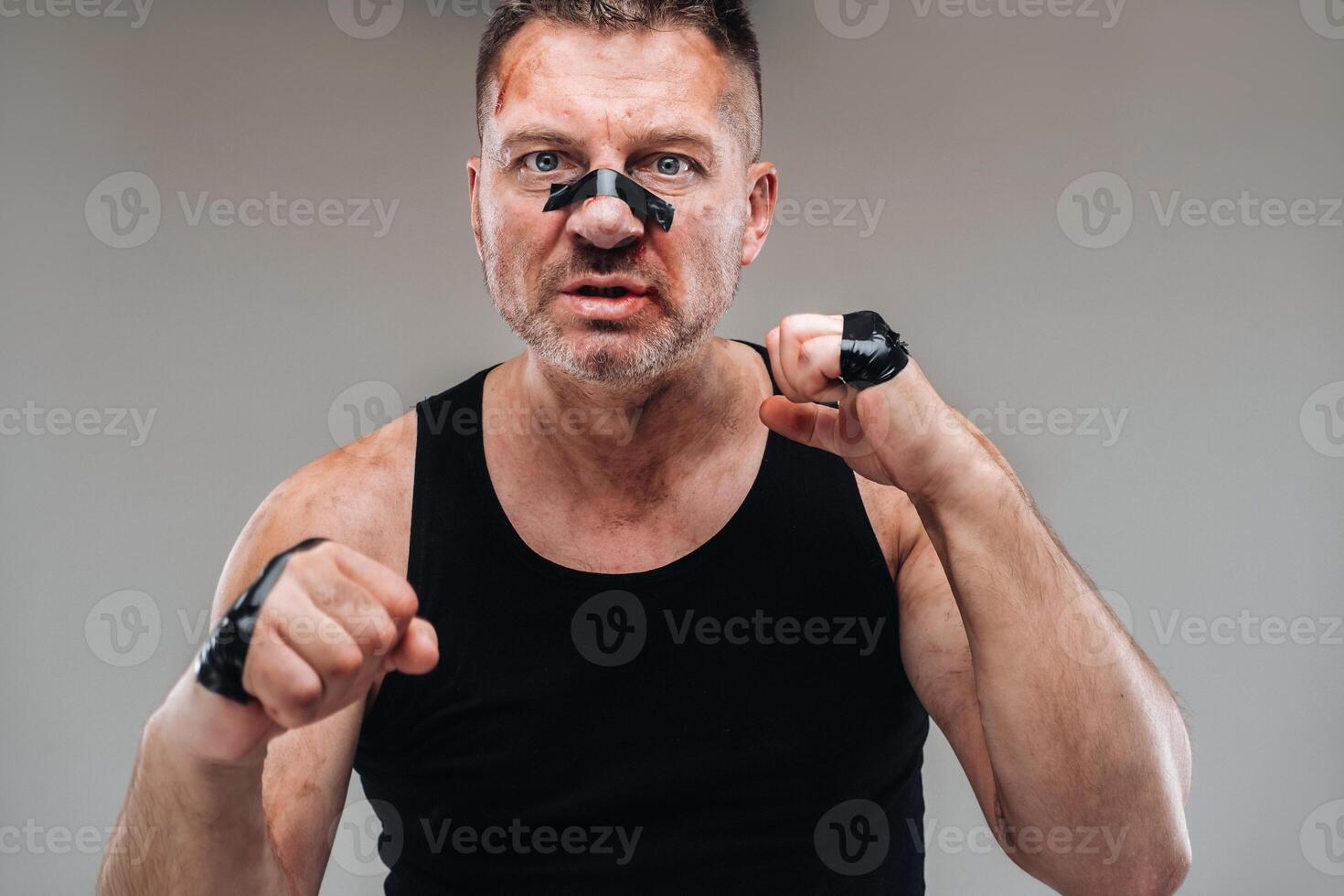 on a gray background stands a battered man in a black T shirt looking like a fighter and preparing for a fight photo