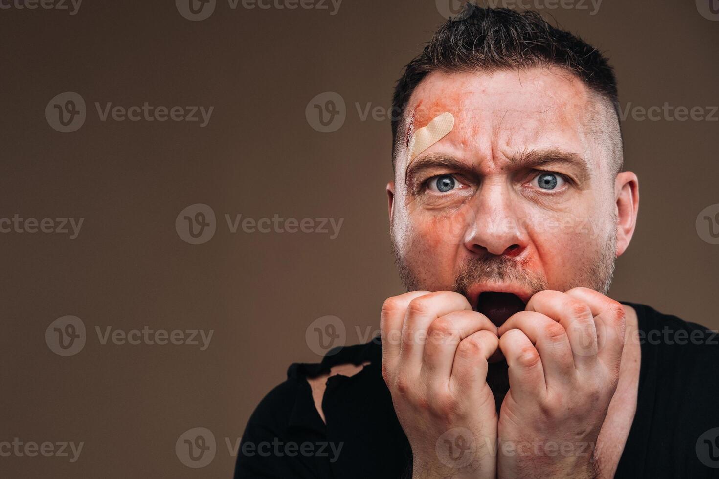 Against a gray background stands a battered angry man in a black T-shirt with wounds photo
