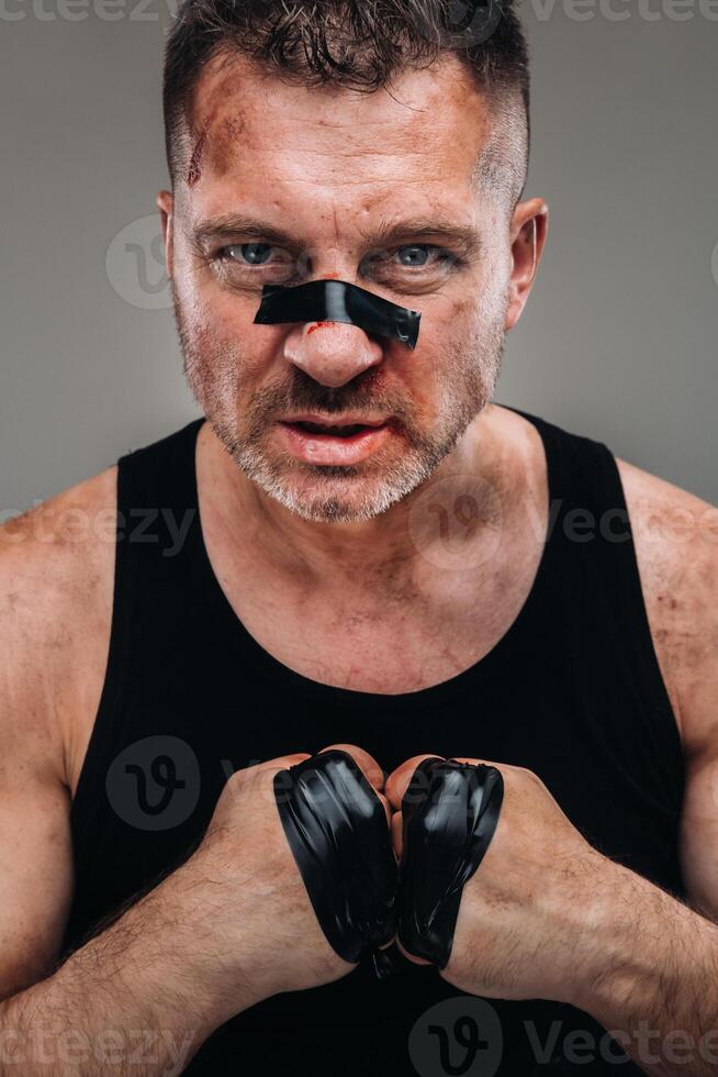 on a gray background stands a battered man in a black T shirt looking like a fighter and preparing for a fight photo