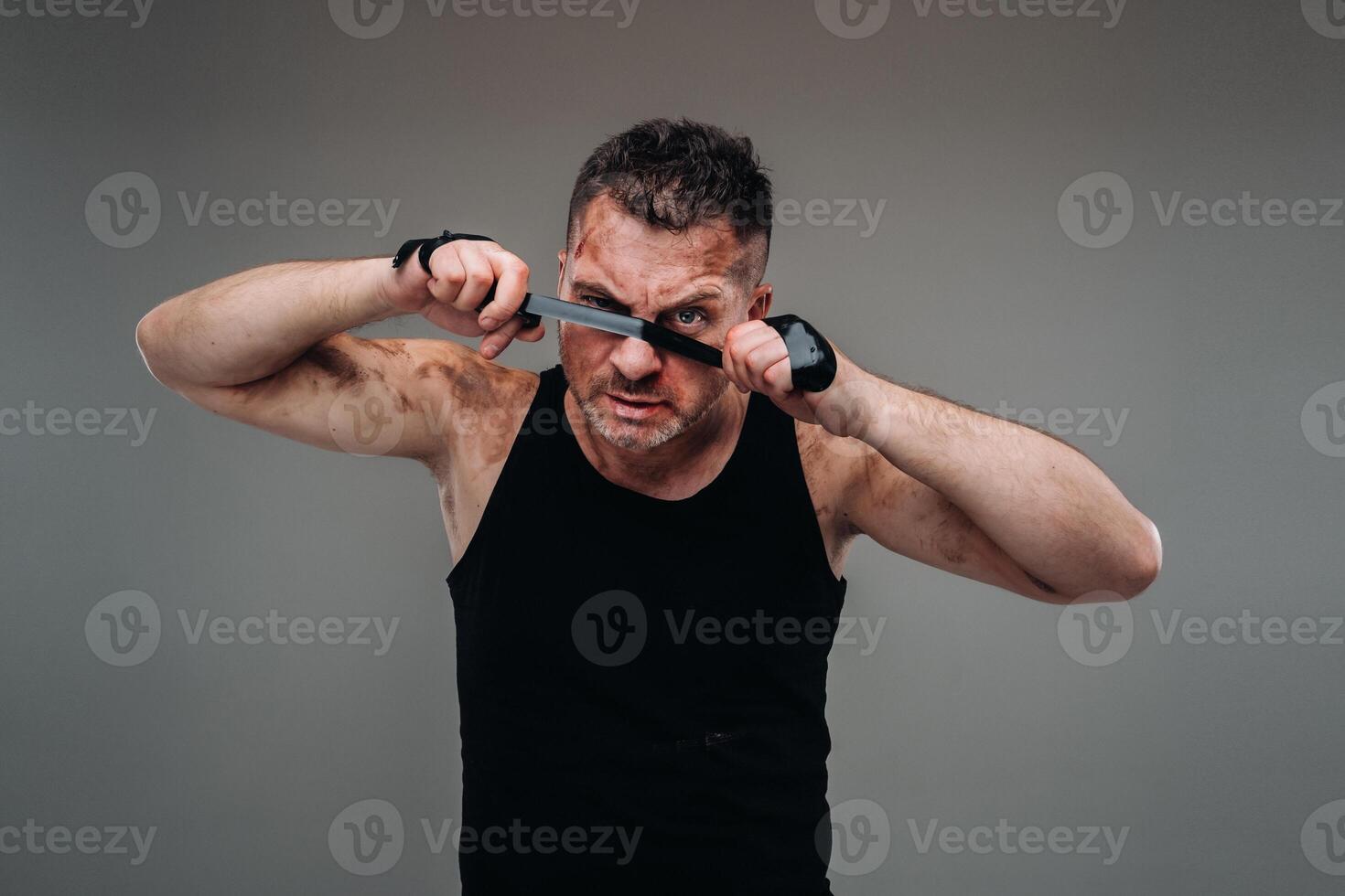 on a gray background stands a battered man in a black T shirt looking like a fighter and preparing for a fight photo