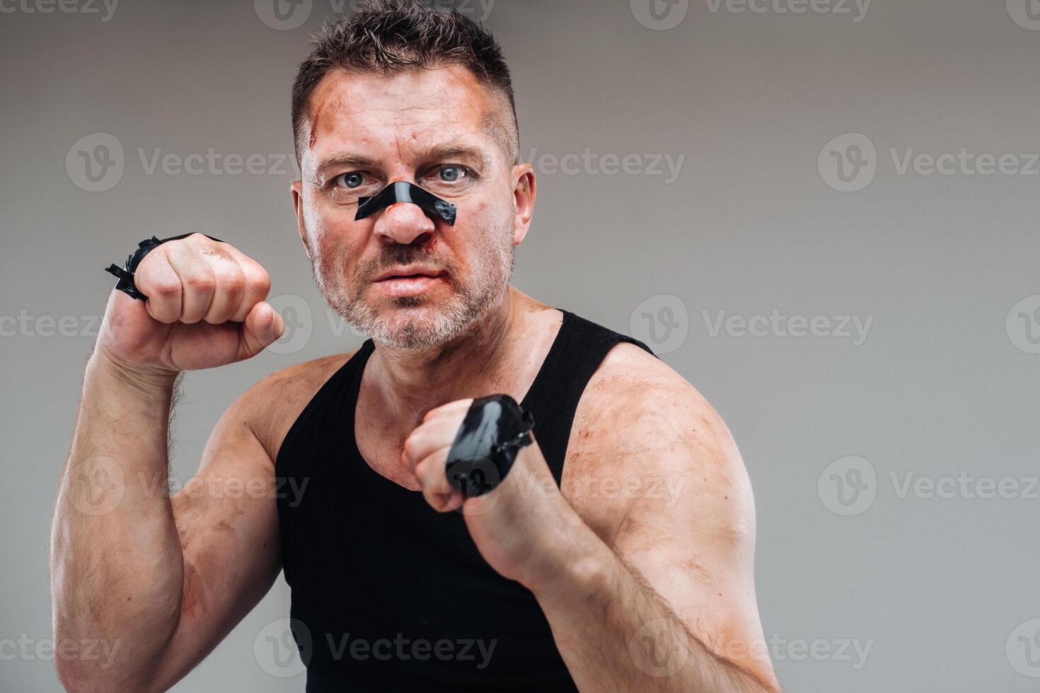 on a gray background stands a battered man in a black T shirt looking like a fighter and preparing for a fight photo