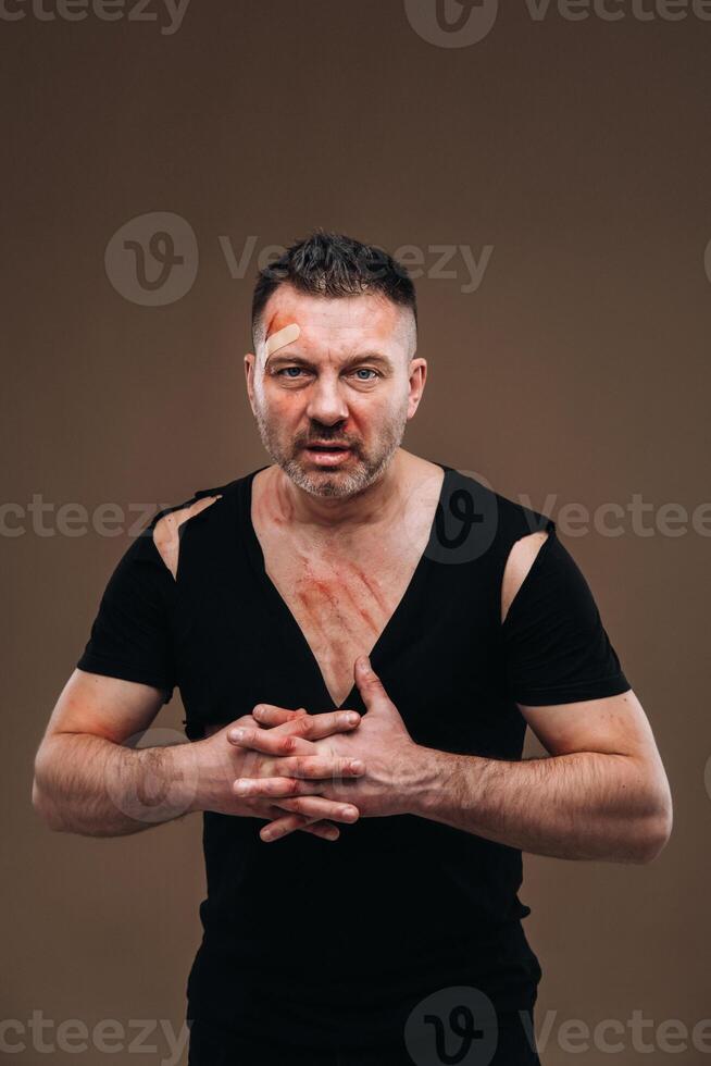 Against a gray background stands a battered angry man in a black T-shirt with wounds photo