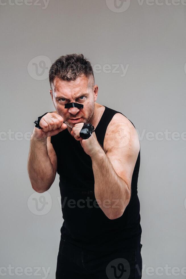 on a gray background stands a battered man in a black T shirt looking like a fighter and preparing for a fight photo