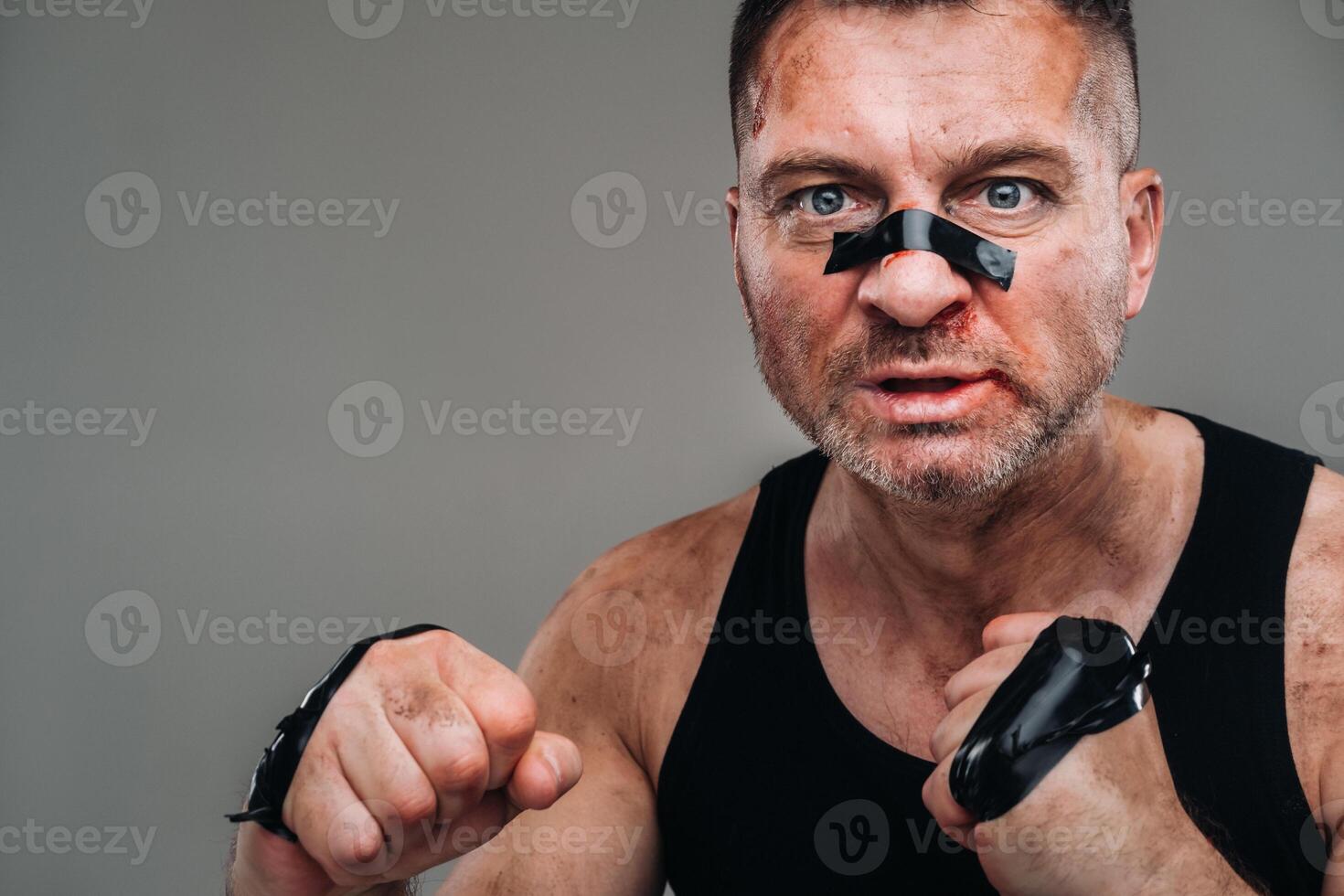 on a gray background stands a battered man in a black T shirt looking like a fighter and preparing for a fight photo
