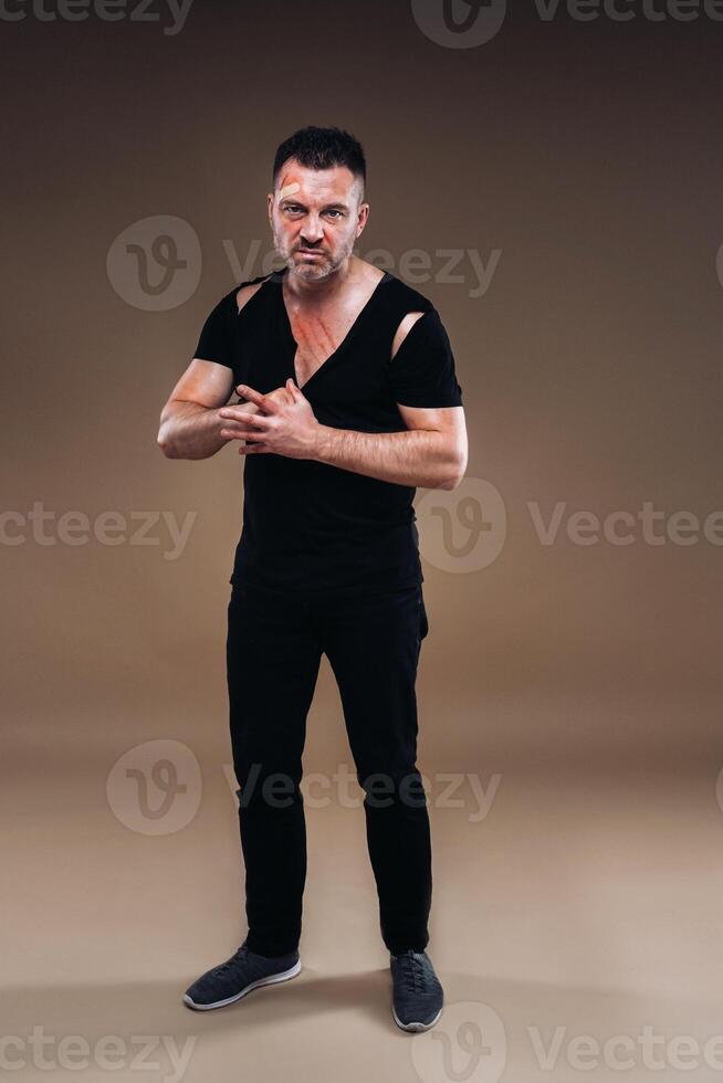 Against a gray background stands a battered angry man in a black T-shirt with wounds photo