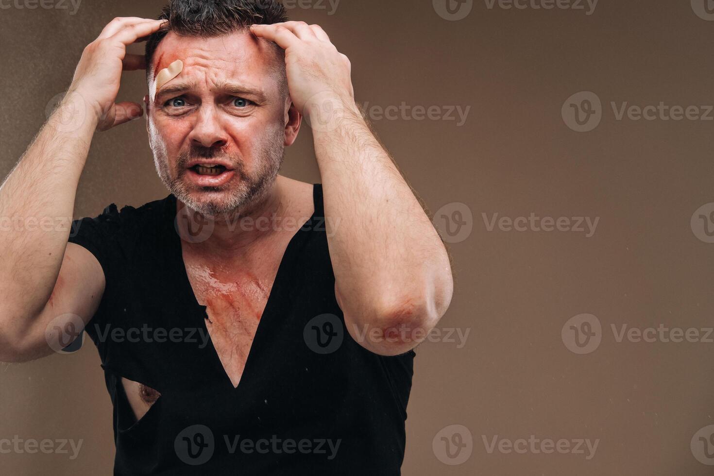 Against a gray background stands a battered angry man in a black T-shirt with wounds photo