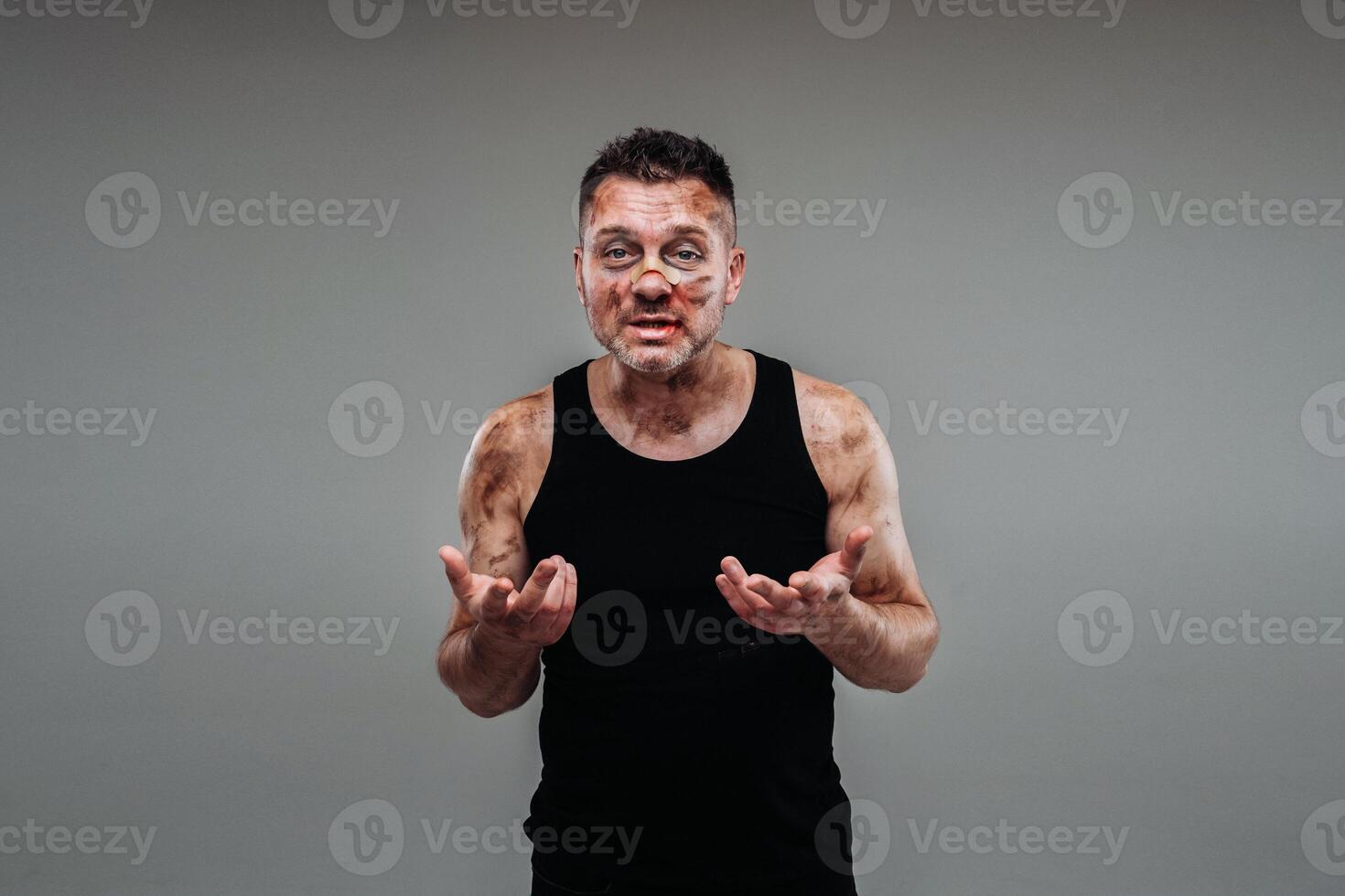 a battered man in a black T shirt who looks like a drug addict and a drunk stands against a gray background photo