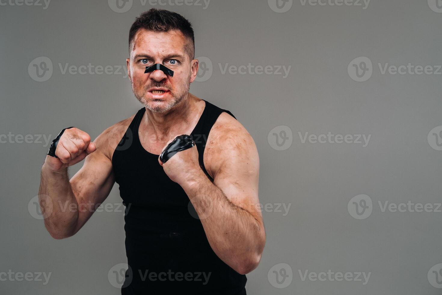 on a gray background stands a battered man in a black T shirt looking like a fighter and preparing for a fight photo