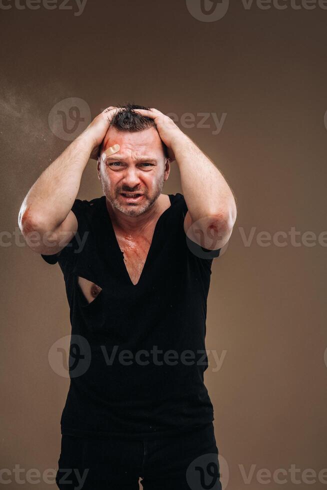 Against a gray background stands a battered angry man in a black T-shirt with wounds photo