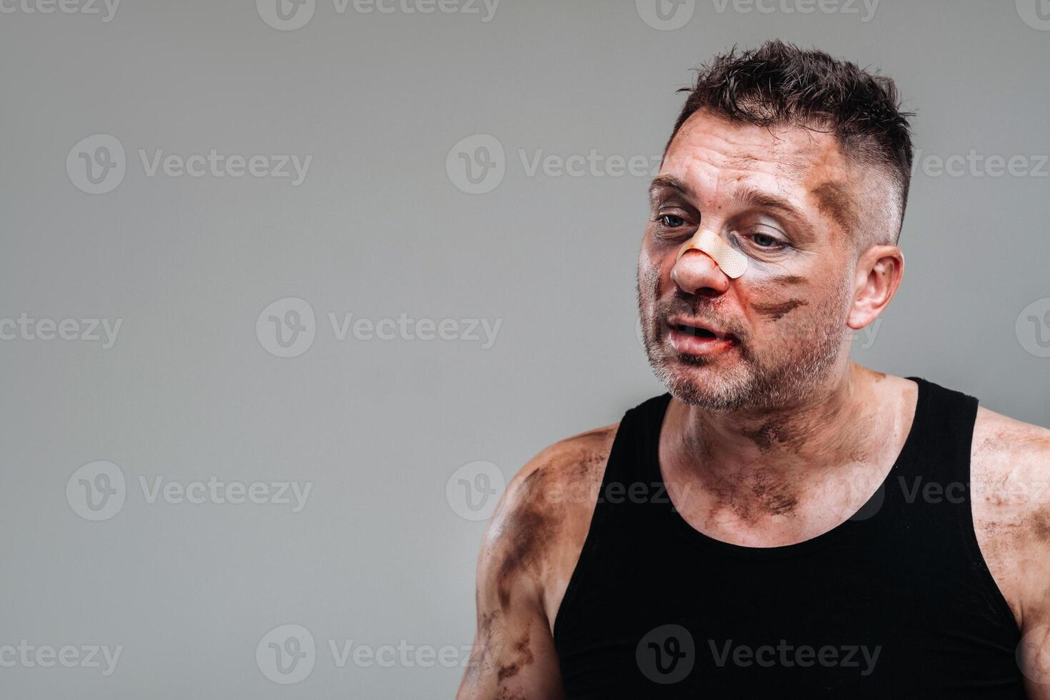 a battered man in a black T shirt who looks like a drug addict and a drunk stands against a gray background photo