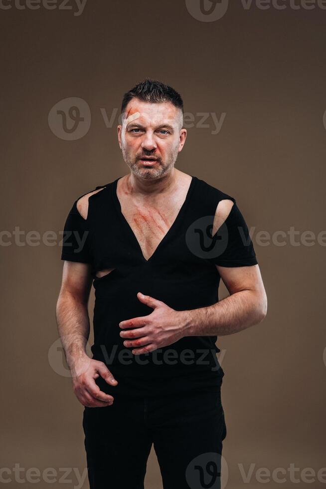 Against a gray background stands a battered angry man in a black T-shirt with wounds photo