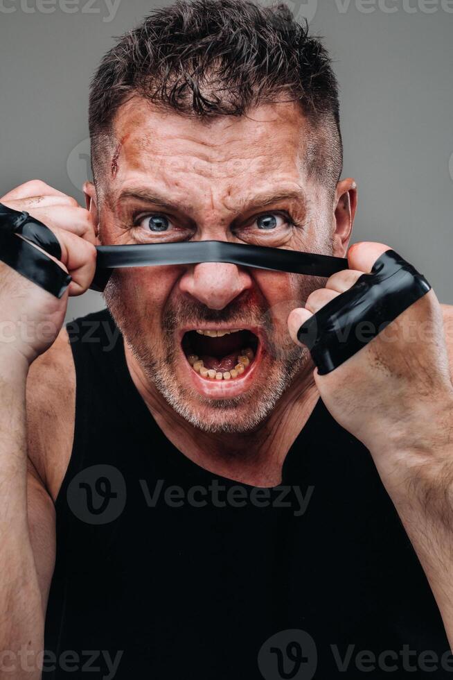 en un gris antecedentes soportes un abollado hombre en un negro t camisa mirando me gusta un combatiente y preparando para un lucha foto