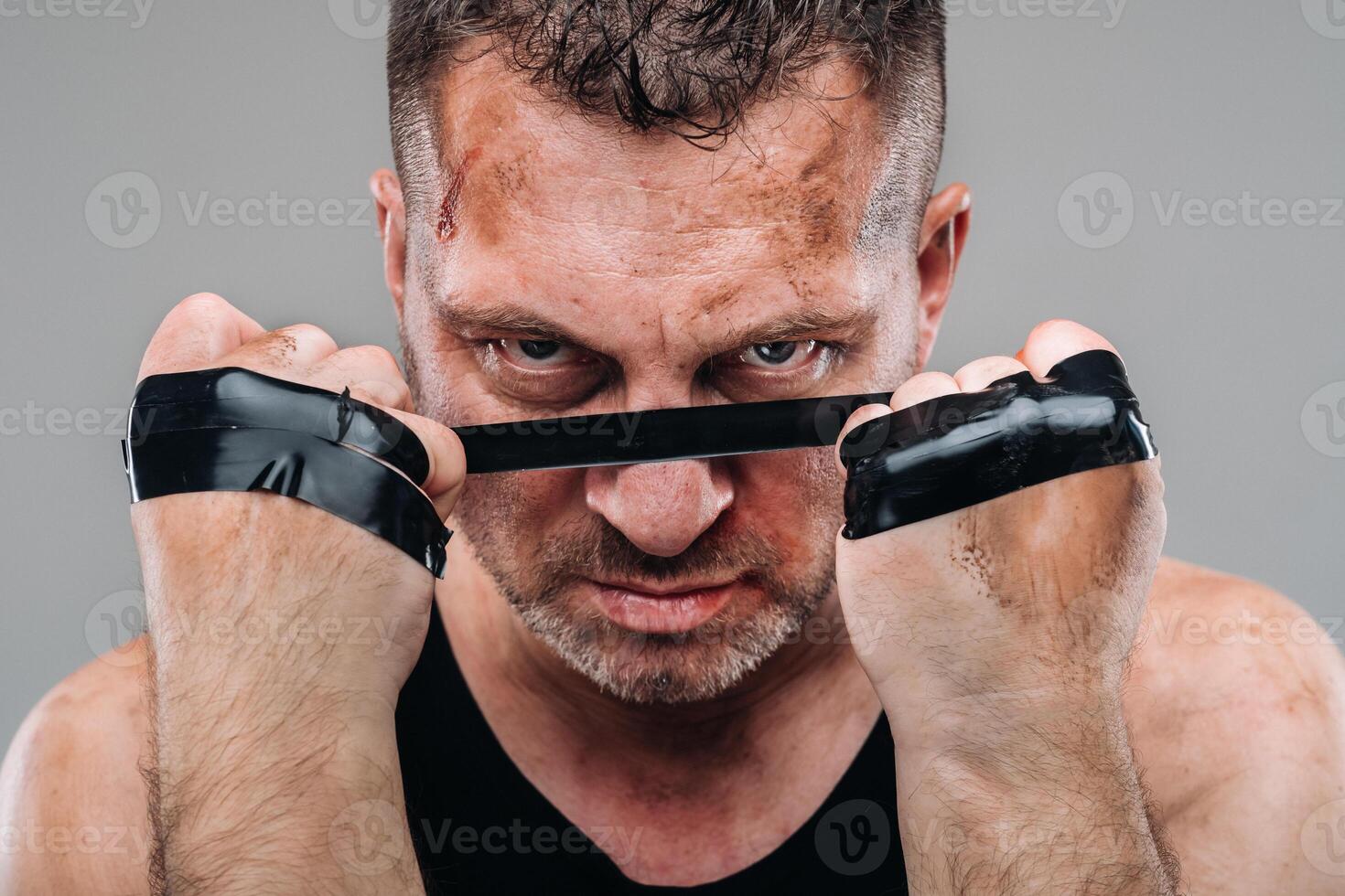on a gray background stands a battered man in a black T shirt looking like a fighter and preparing for a fight photo