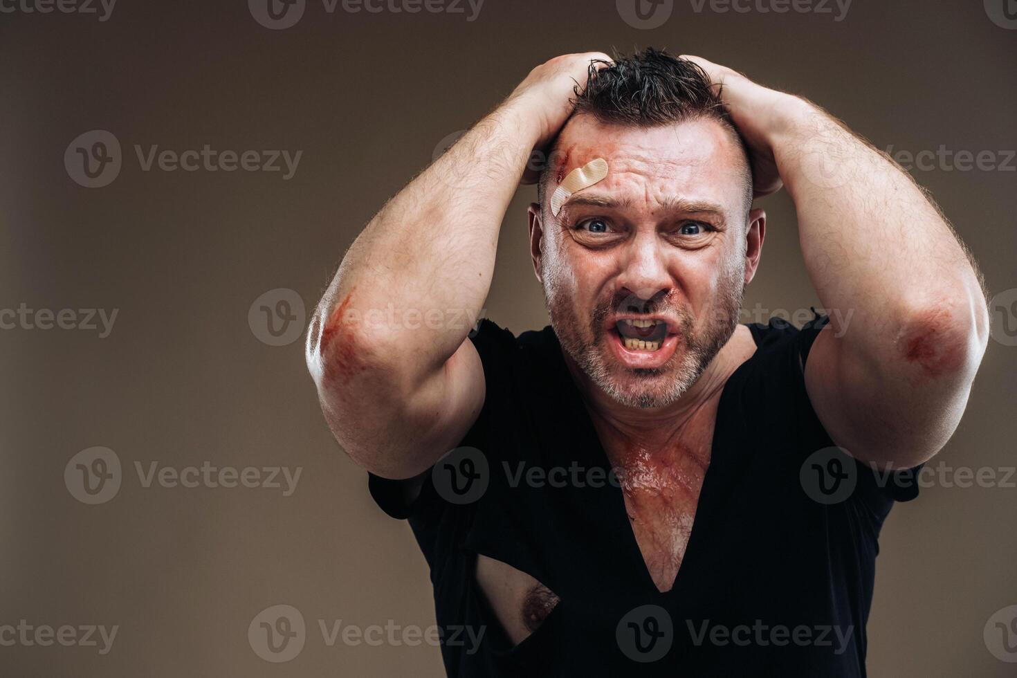 Against a gray background stands a battered angry man in a black T-shirt with wounds photo