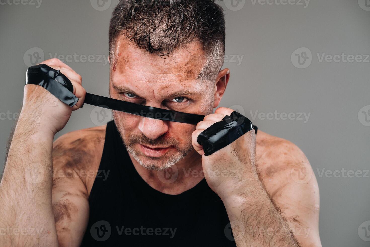 on a gray background stands a battered man in a black T shirt looking like a fighter and preparing for a fight photo