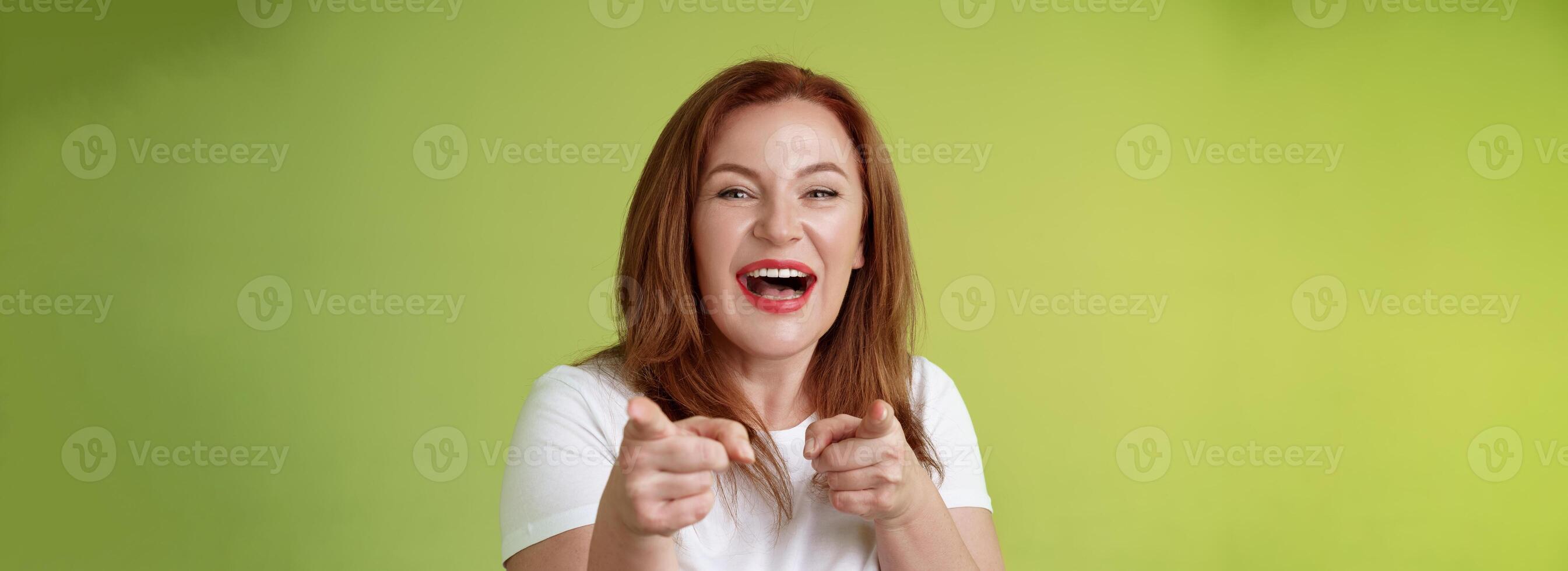 You did best. Friendly joyful enthusiastic redhead ginger middle-aged female pointing index fingers camera finger pistol gesture smiling broadly congratulate cheer coworker stand green background photo