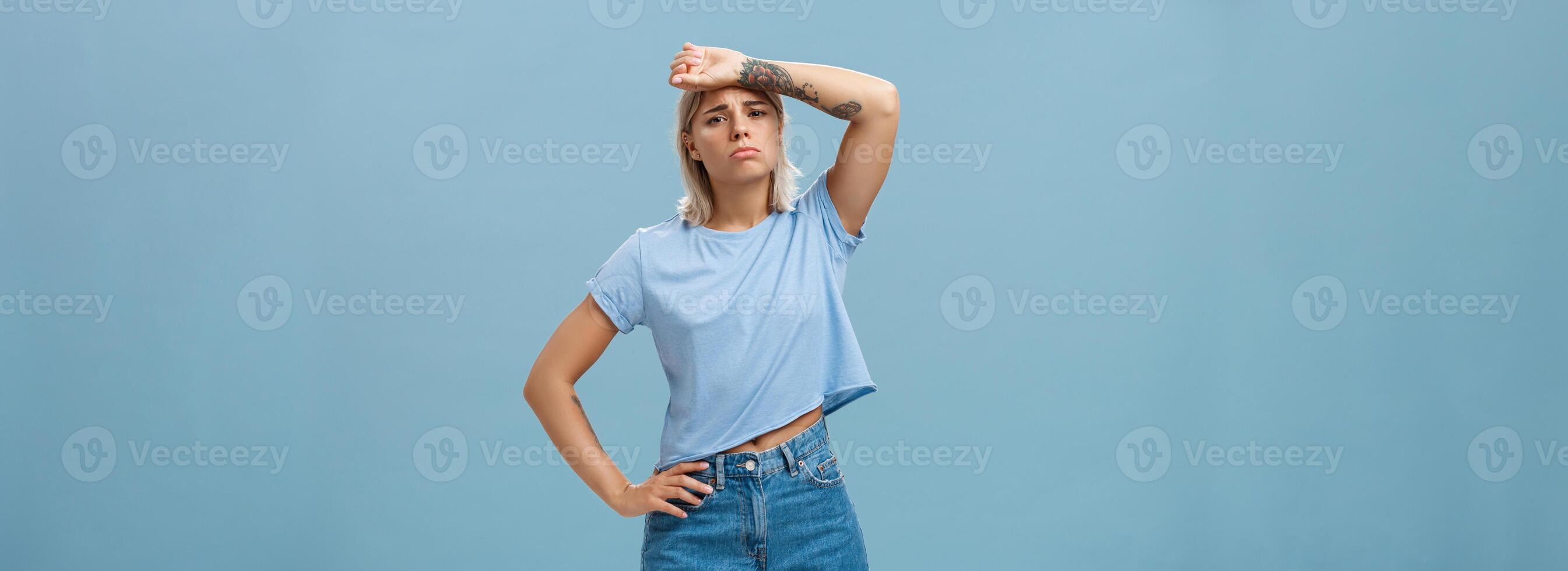 Tired need help save me from work. Gloomy displeased exhausted young sportswoman with tattoos and tanned skin whiping sweat from forehead gazing upset at camera being fed up of problems photo