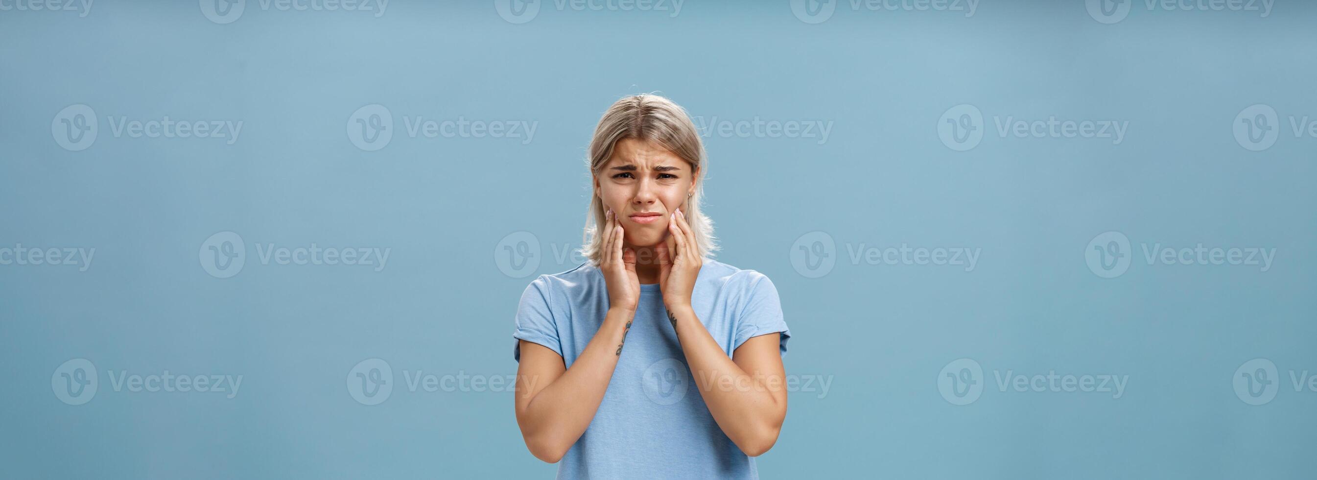 Girl feeling pain in teeth after drinking hot coffee. Displeased unhappy troubled young girl with blond hair frowning feeling discomfort in mouth holding hands on cheeks suffering toothache photo