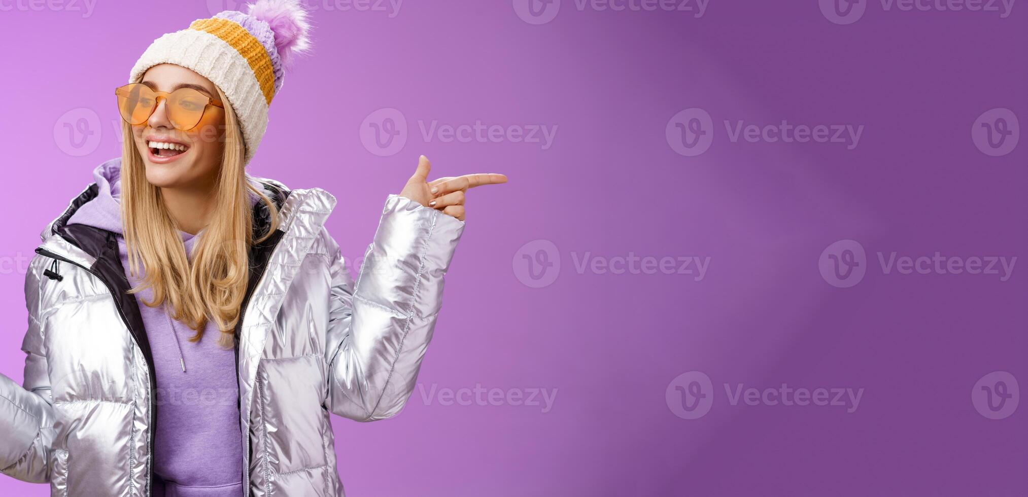 Cool sassy friendly-looking blond girl pointing different sides right left choose which way go look delighted carefree enjoy awesome winter vacation wear stylish silver jacket, hat sunglasses photo