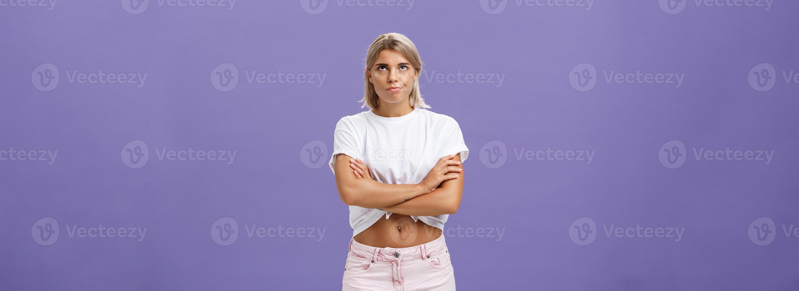 Girl being irritated waiting for appointment sighing rolling eyes up from annoyance crossing hands over body and smirking from impatience and dissatisfaction standing intense over purple wall photo